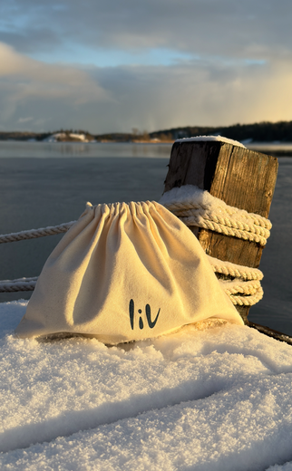 Drawstring bag with 'liv' branding on a snowy surface near a body of water.