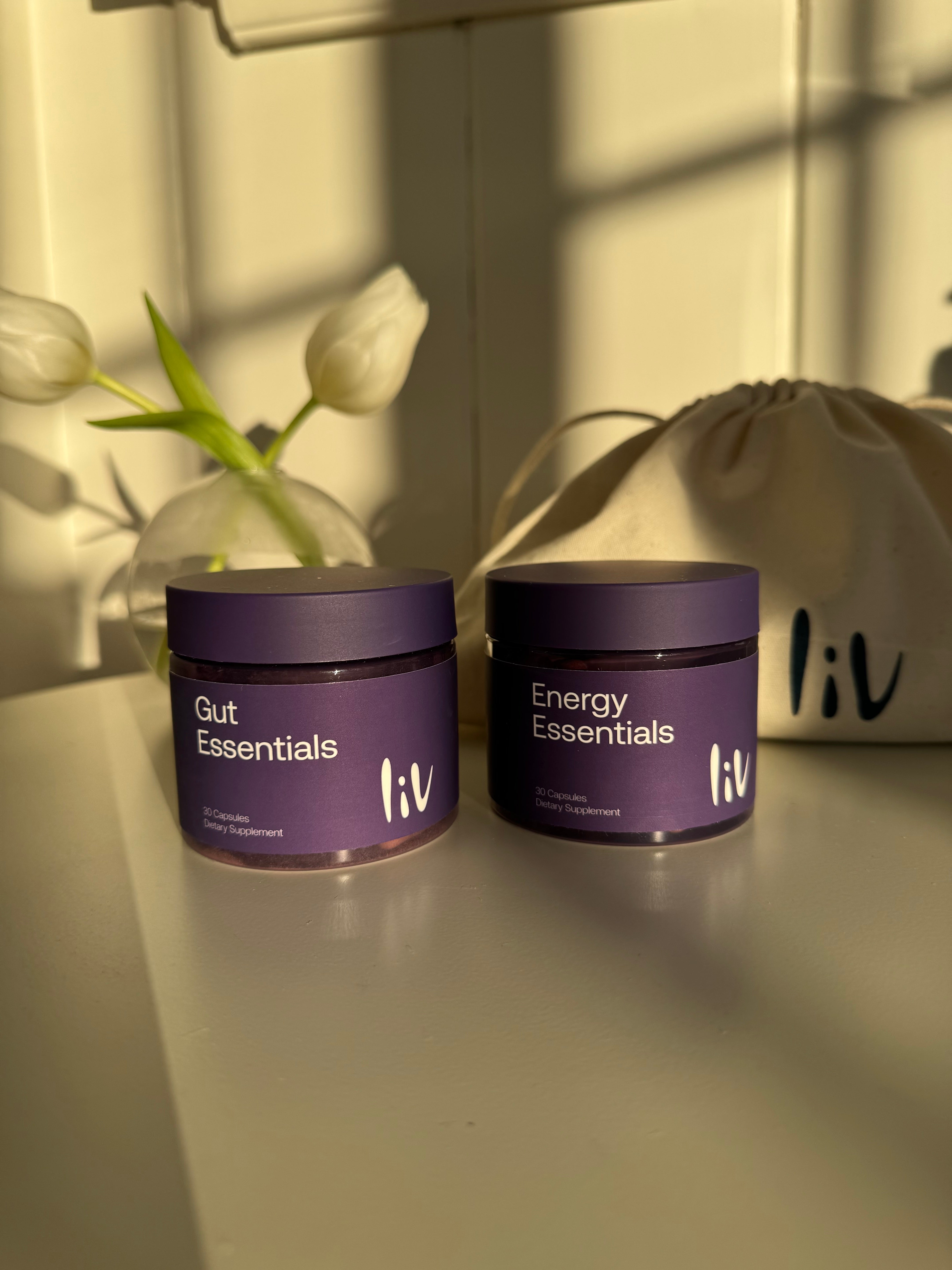 Two purple containers labeled 'Energy Essentials' on a neutral background with a flower.