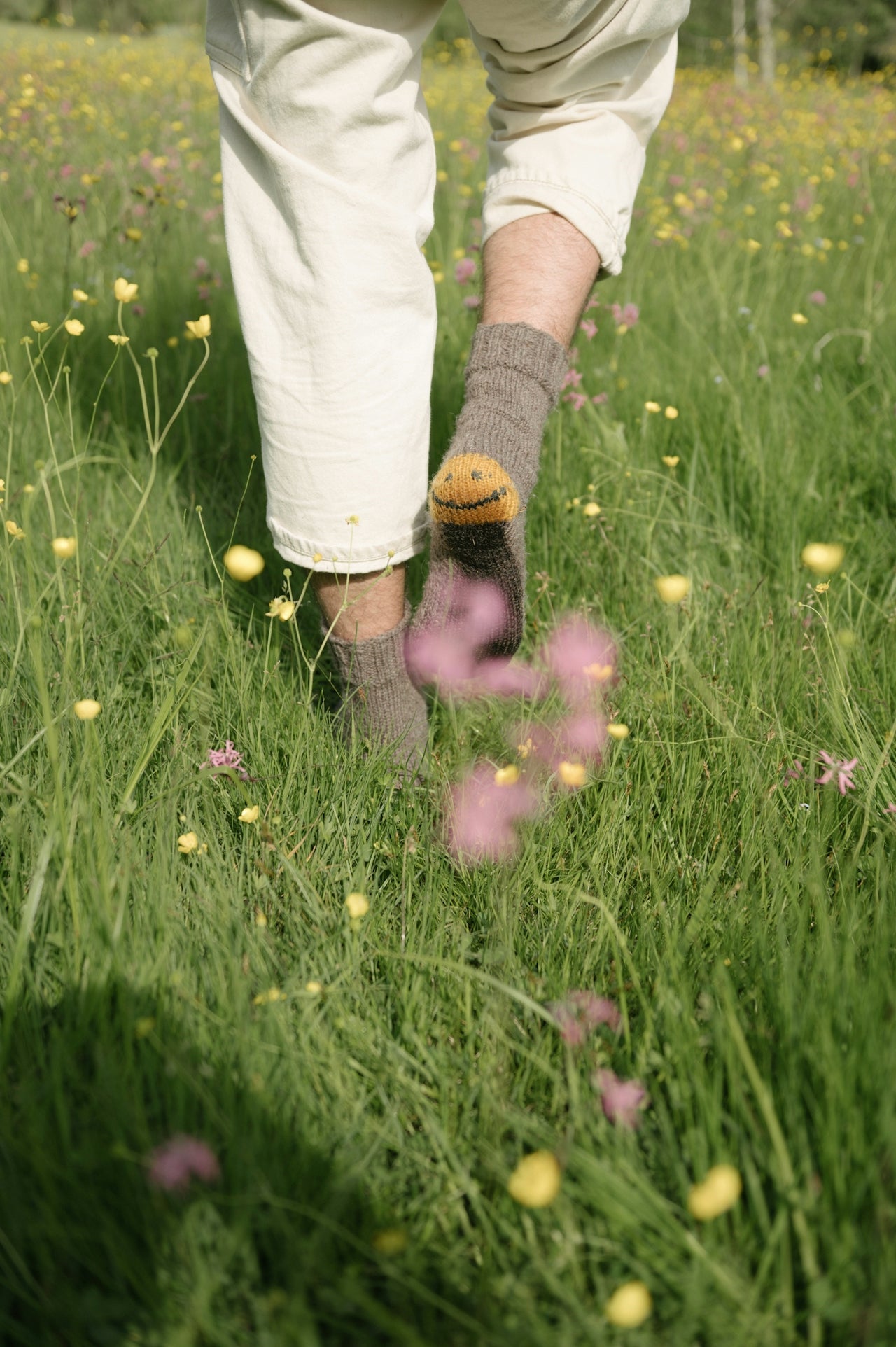 Person wearing white pants and gray socks walking through a field of wildflowers.