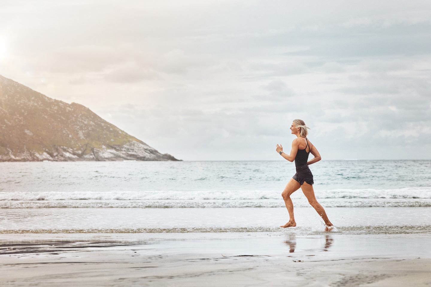 Woman running on a beach with mountains in the background