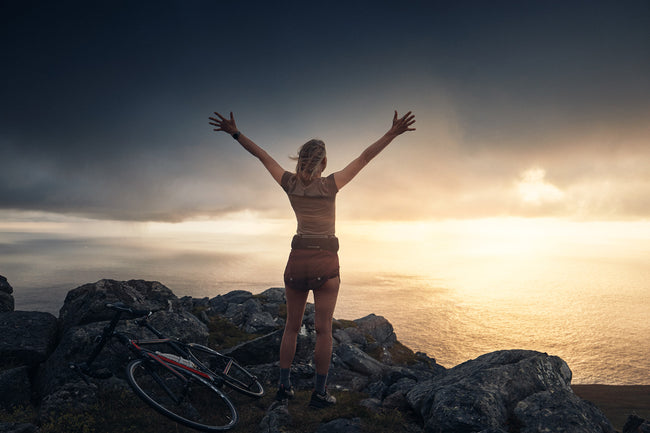 Person with arms outstretched on a rocky mountain top at sunset