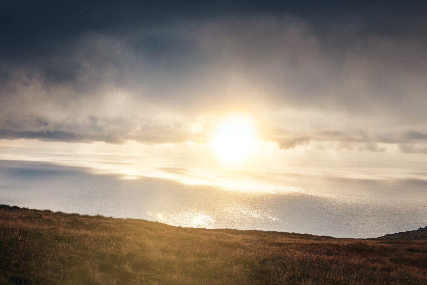 Sunrise or sunset over a coastal landscape with clouds and water.
