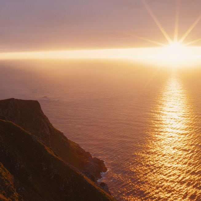 Sunset over a cliff overlooking the ocean with warm colors.