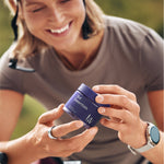 Woman on a bicycle holding a blue container with a brand logo, wearing a helmet.