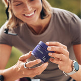 Woman on a bicycle holding a blue container with a brand logo, wearing a helmet.