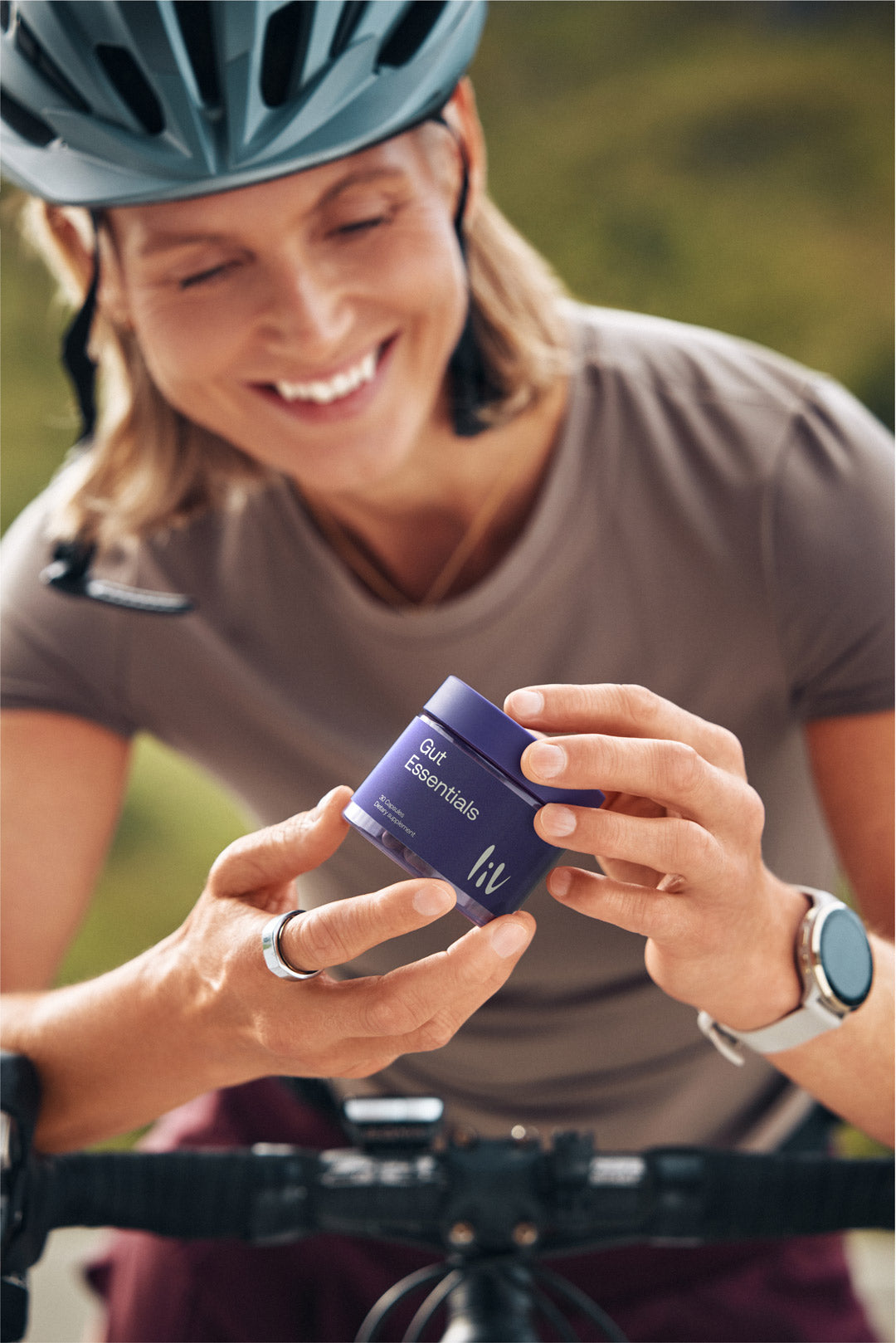 Woman on a bicycle holding a blue container with a brand logo, wearing a helmet.
